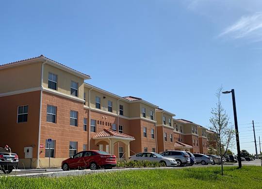 A red car is parked in front of a building with a parking lot.
