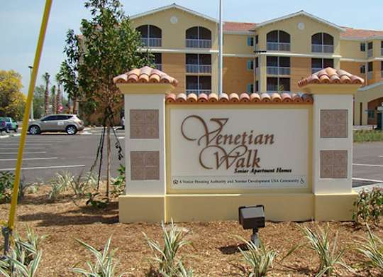 A sign for Venetian Walk Apartment Homes stands in front of a building.