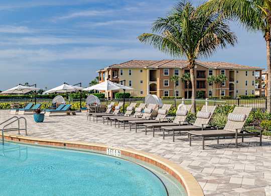 A pool area with lounge chairs and palm trees in front of a building.