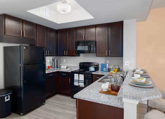 A kitchen with a black refrigerator and brown cabinets.