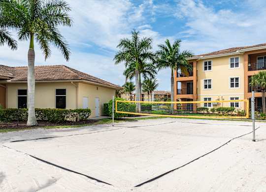 A tennis court is in the foreground of a residential area with apartment buildings and palm trees.
