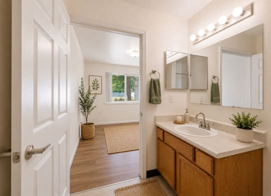 A bathroom with a white door, a brown counter, and a mirror with lights above it.
