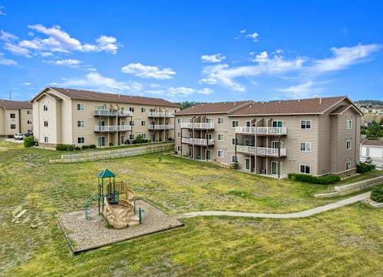 A playground with a slide and swings is in the foreground of a large apartment complex.