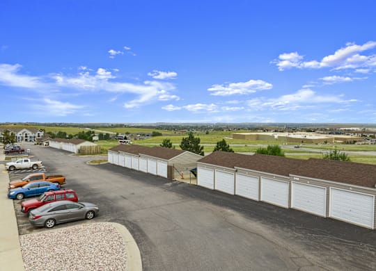 A parking lot with cars and a long row of garages.