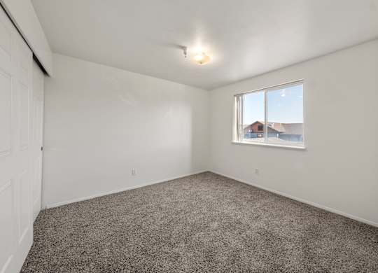 A room with a carpeted floor and a window showing a view of a house.