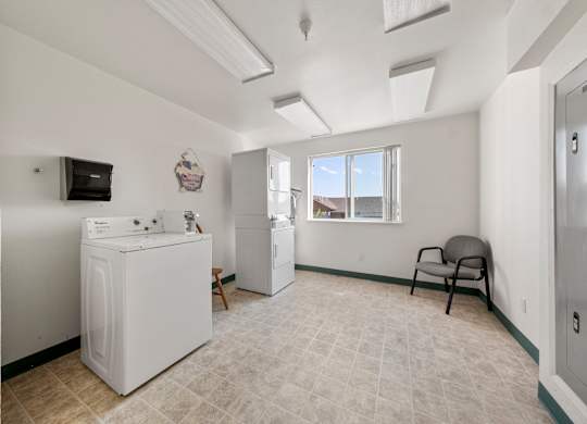A laundry room with a washer and dryer, a chair, and a window.