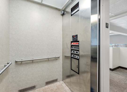 A stainless steel elevator with a black control panel and a white wall.