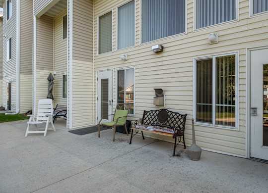 A patio with a bench and chairs outside a house.