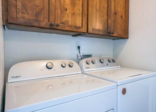 A white washing machine and dryer are sitting under a wooden cabinet.