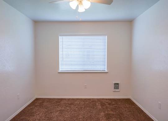 A room with a ceiling fan and a window with blinds.
