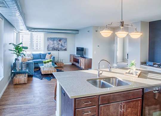 A kitchen with a large island and a living room with a couch and a plant.
