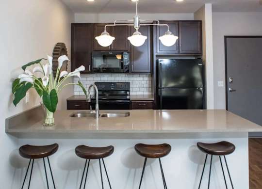 A kitchen with a white countertop and brown bar stools.
