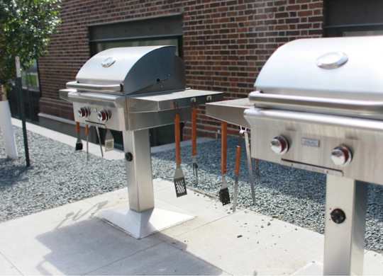 Two silver barbecue grills are placed on a gravel surface.