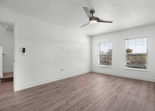 an empty living room with a ceiling fan and two windows