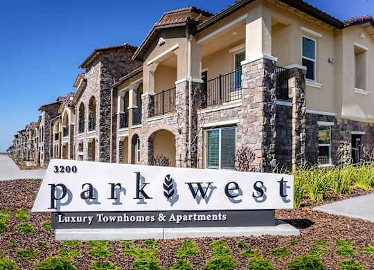A sign for Parkwest Luxury Townhomes & Apartments is in front of a building.