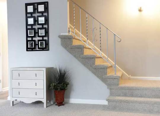 A staircase with a metal railing and a potted plant next to a white chest of drawers.