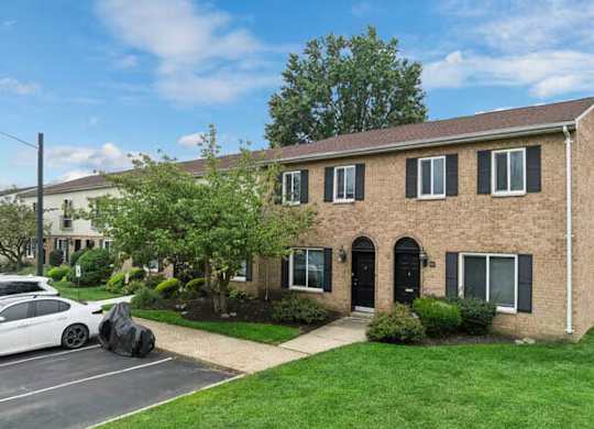 A white car is parked in front of a brick house.