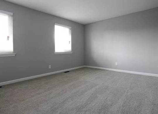 A room with grey walls and carpeted floor with two windows.