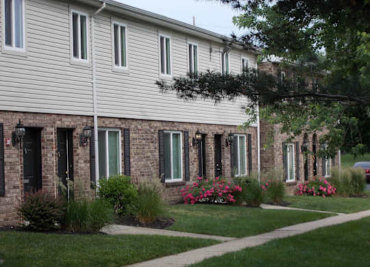 A building with a white siding and a brick facade with windows and flower beds in front.