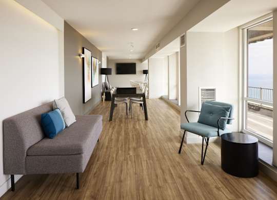 A grey couch with a blue pillow sits in a room with wooden floors and white walls.