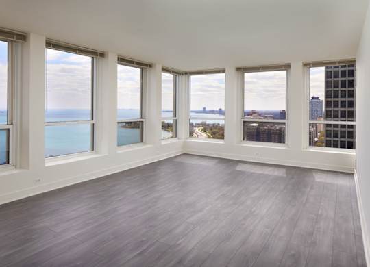 A large empty room with wooden floors and windows overlooking a body of water.
