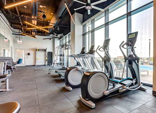 A gym with a row of stationary bikes and a fan overhead.