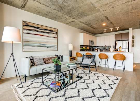 A modern living room with a glass coffee table and a large abstract painting on the wall.