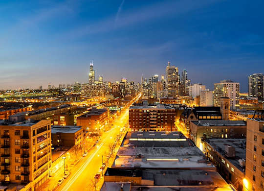 A cityscape at dusk with buildings and streets illuminated.