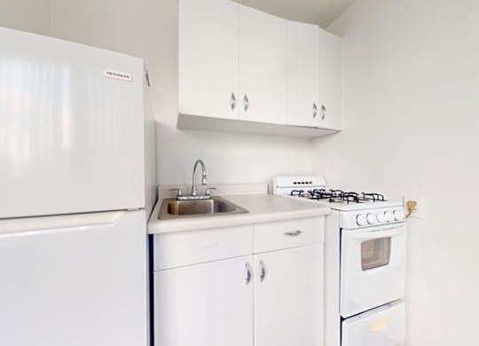 A white kitchen with a fridge, stove, and sink.