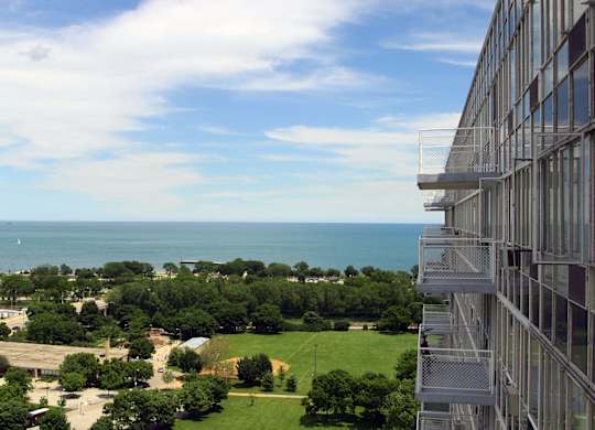A view from a high-rise building looking down at a green field and a body of water.