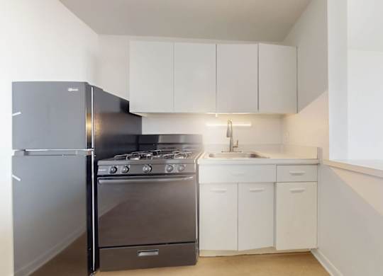 A kitchen with a black fridge, stove and white cabinets.