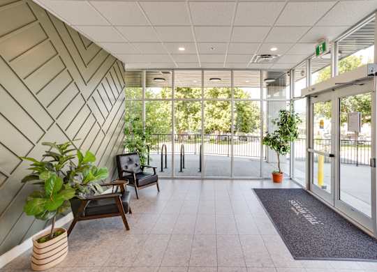 A hallway with a bench, potted plants, and a door.