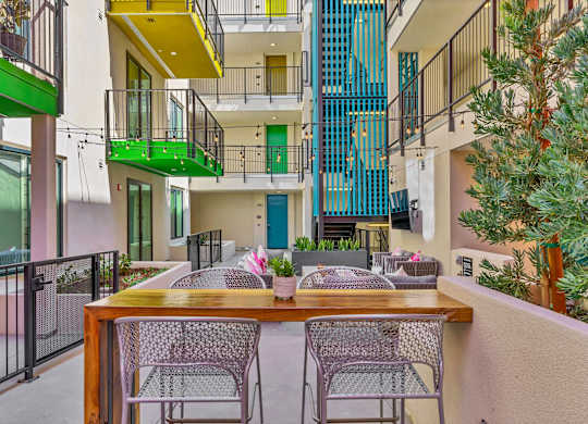 A patio with a table and chairs overlooks a courtyard with a fence and a tree.