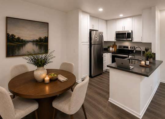 A dining room with a wooden table and chairs, a fridge, a microwave, and a painting on the wall.