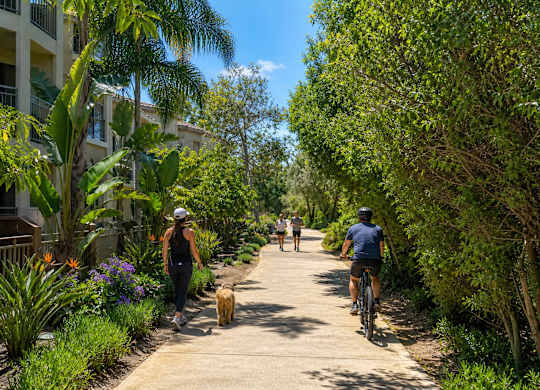 A woman walking a dog on a path with a man riding a bike behind her.