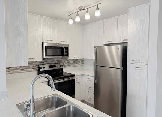 A kitchen with a stainless steel refrigerator and a sink with a faucet.