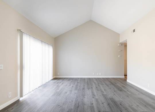 A room with a wooden floor and a window with white curtains.