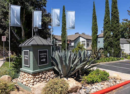 A sign for a leasing office is in front of a building with a landscaped area.