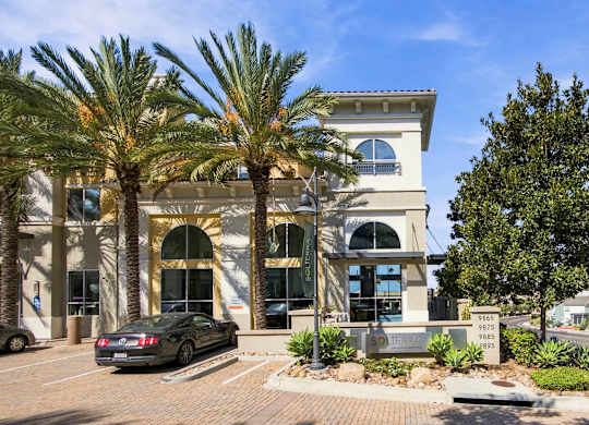 A car is parked in front of a building with palm trees.