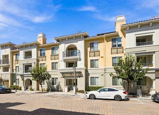 A row of apartment buildings with cars parked in front.