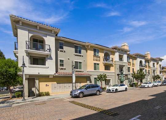A row of apartment buildings with cars parked in front.
