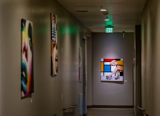 A hallway with a green exit sign and artwork on the walls.