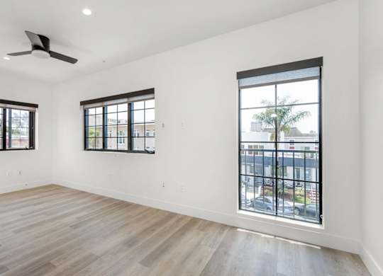 A spacious room with wooden floors and two windows.