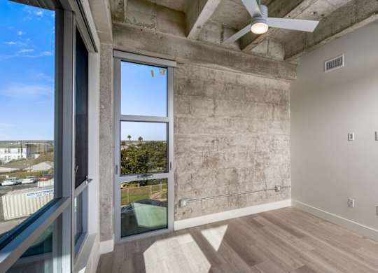 A room with a ceiling fan and a window overlooking a parking lot.