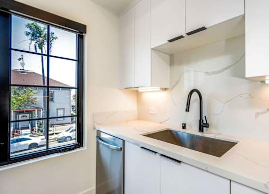 A kitchen with a white counter top and a window overlooking a street.