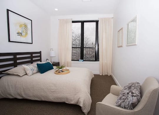A bedroom with a bed, chair, and window.