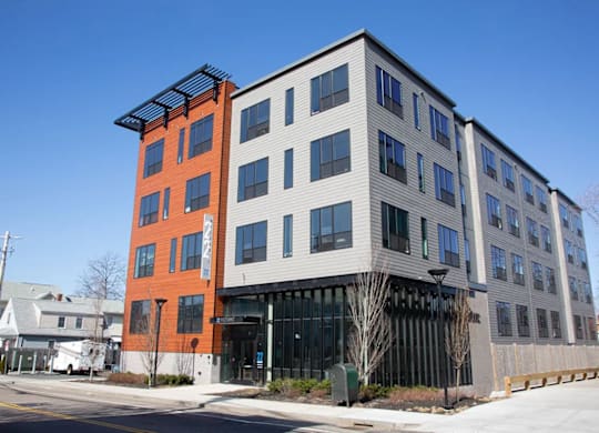 A modern building with a red and grey facade stands on a street corner.