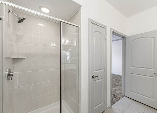 A white bathroom with a glass shower door and a white tiled shower wall.