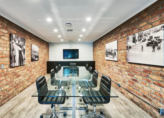 a conference room with a glass table and chairs and an exposed brick wall at The Meadows Apartments, Culver City , CA