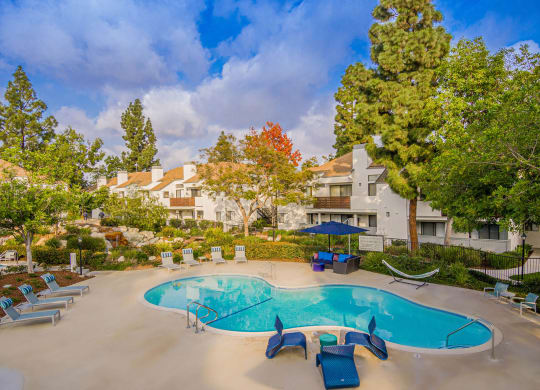 a swimming pool with chairs and umbrellas in front of a building at Sendero Huntington Beach, Huntington Beach, CA